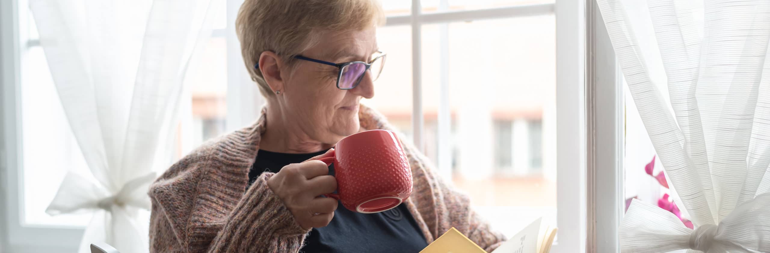 elderly woman reading book while sipping tea